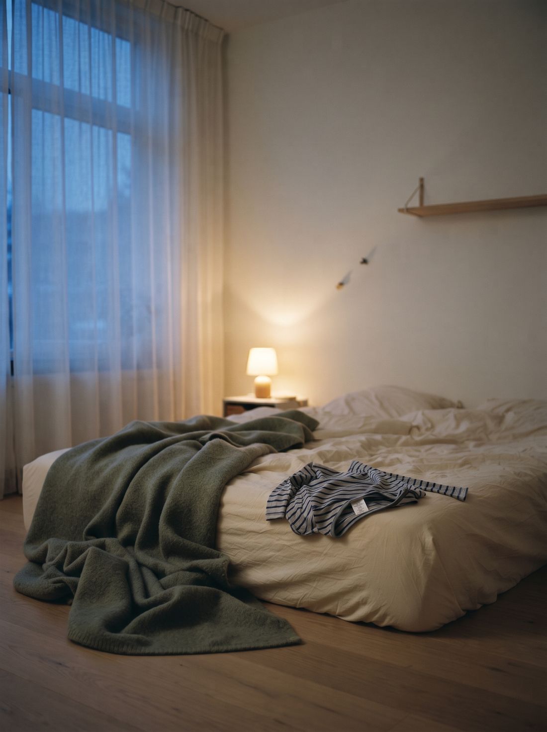 Una cama infantil desarreglada al atardecer, con un pijama al revés sobre las sábanas, sin nadie en la escena.
